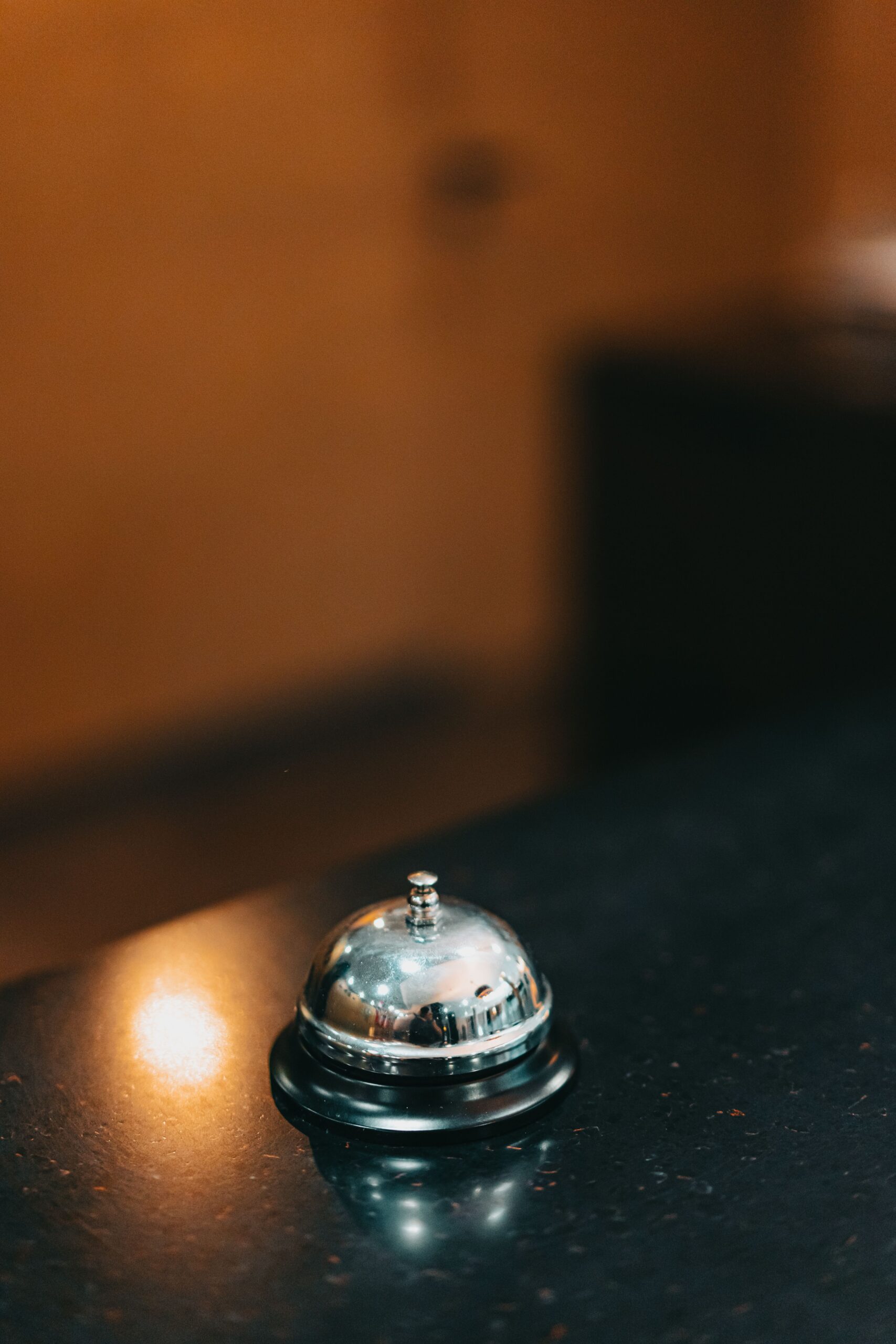 A shiny metal call bell on a dark counter in a hotel reception area with a blurred background.